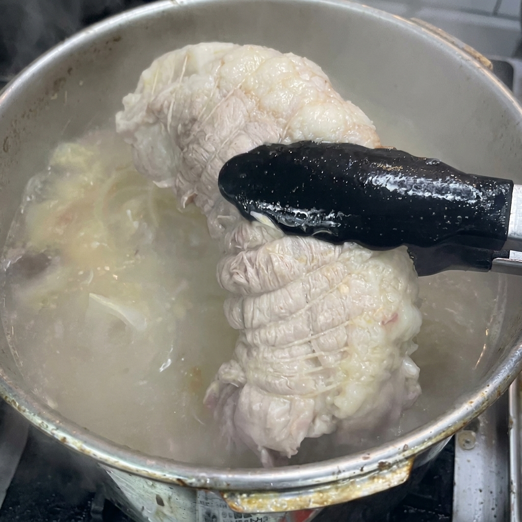 Des pinces sortant un morceau de porc cuit et ficelé dune marmite de bouillon bouillonnant.