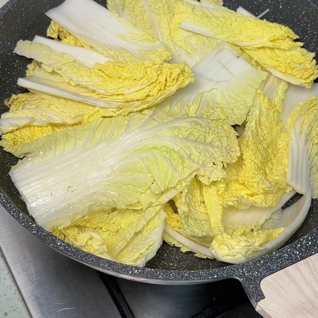 Une poêle remplie dingrédients avec une grosse cuillère de pâte de piment rouge au centre, en cours de remplissage avec un bouillon.