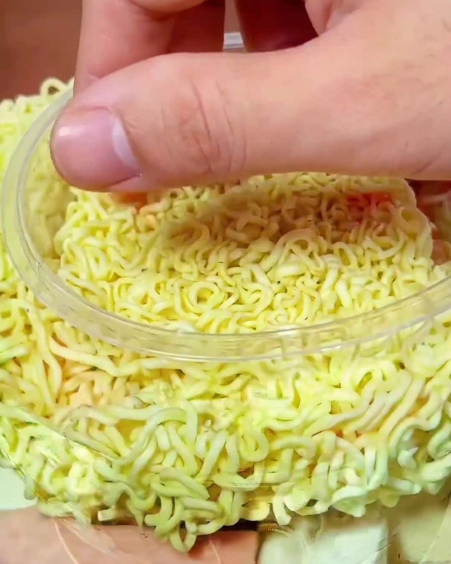 Une main déposant des morceaux de kimchi rouge vif sur les nouilles dans la marmite.