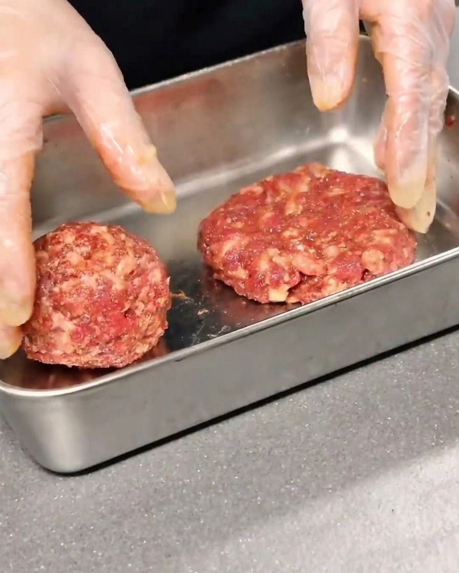 Deux steaks de bœuf assaisonnés façonnés et aplatis dans un récipient en métal.