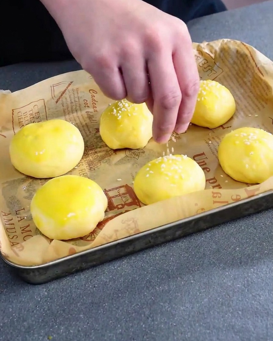 Graines de sésame blanc saupoudrées sur des pains à burger crus et dorés à lœuf.