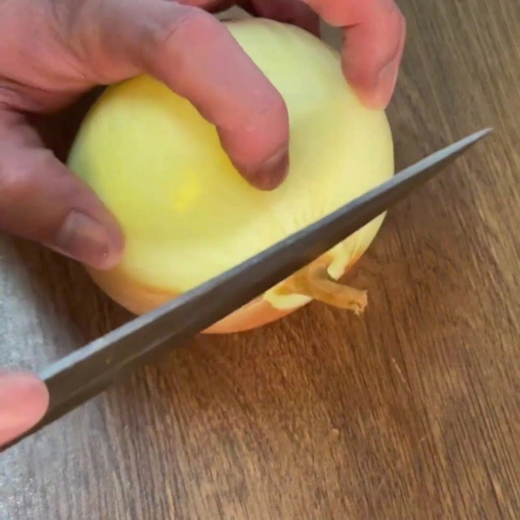 Mains utilisant un couteau pour couper la racine dun oignon jaune pelé sur une planche à découper en bois.