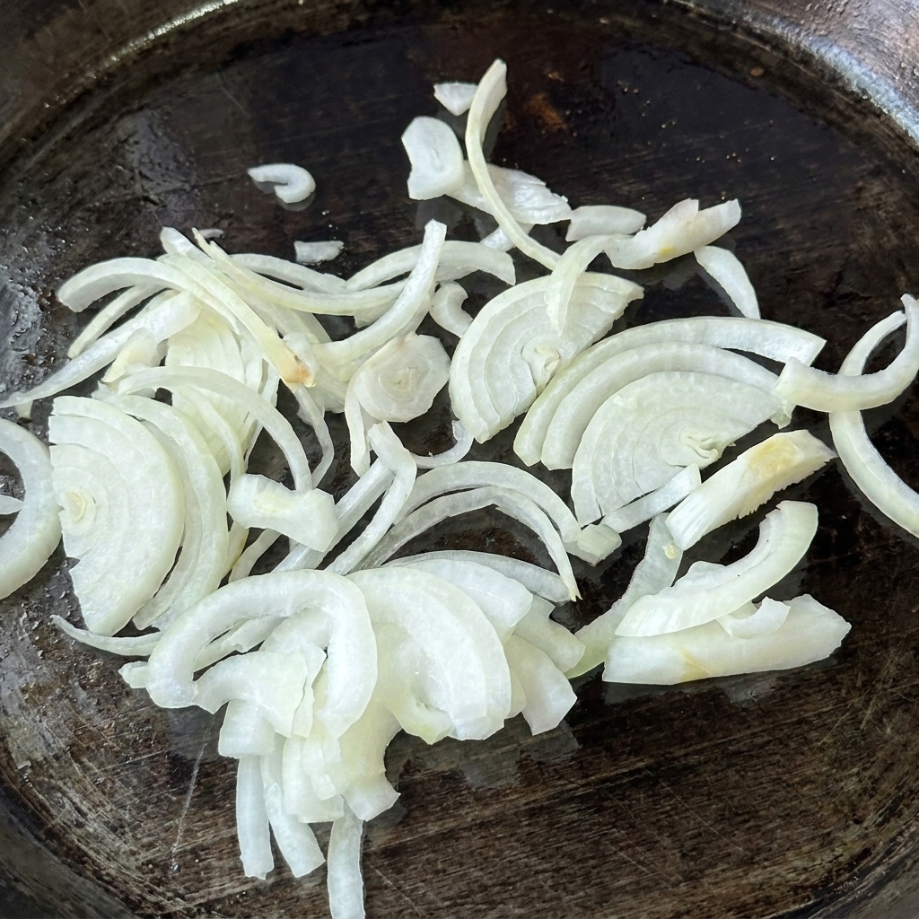 Un monticule doignons blancs crus et finement tranchés posés sur une plancha graissée et chaude.