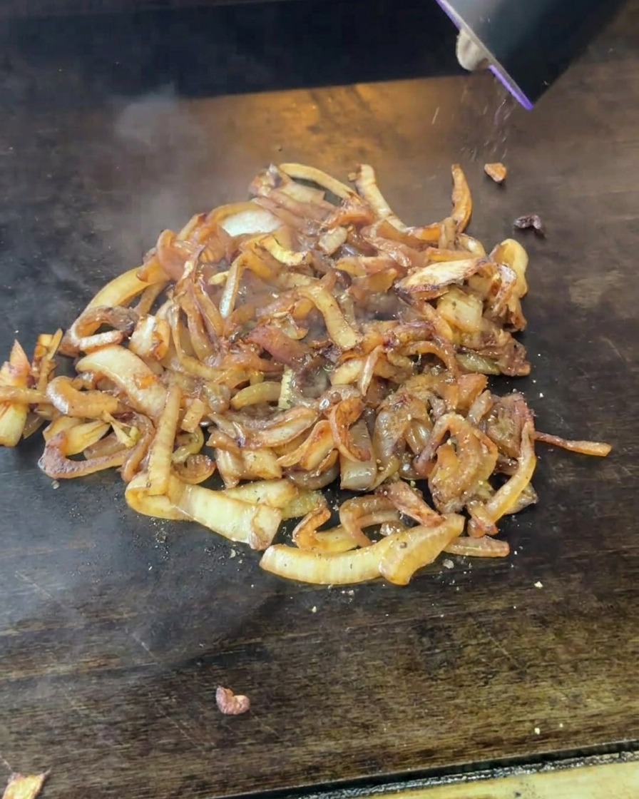 Un moulin électrique saupoudrant du poivre noir fraîchement moulu sur un tas doignons fondants et caramélisés.
