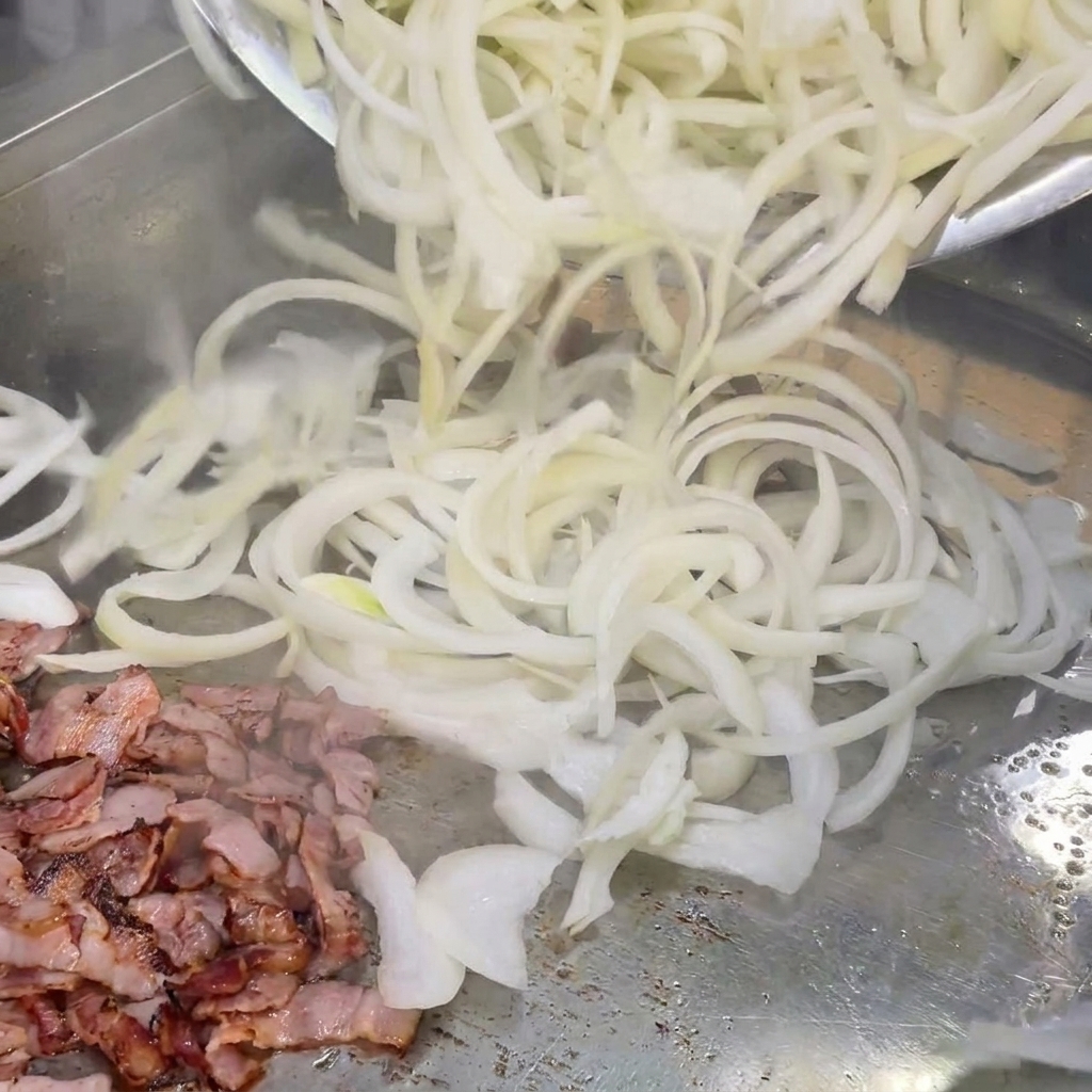 Oignons blancs fraîchement tranchés mélangés avec des morceaux de bacon sur une plaque chaude.