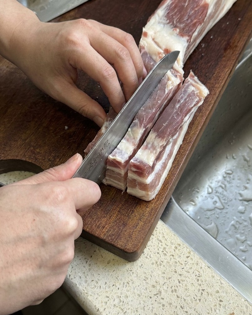 La poitrine de porc crue découpée en longues bandes épaisses avec un couteau de cuisine bien aiguisé.