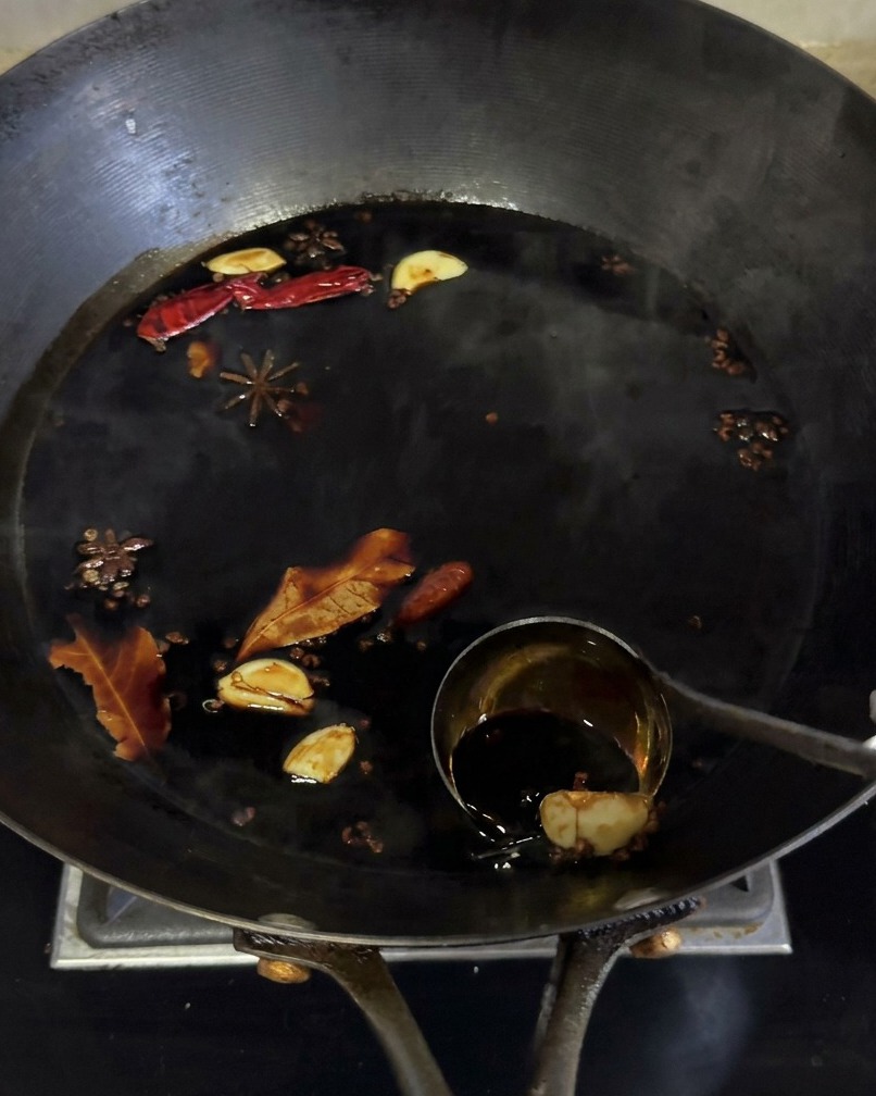 La marinade à la sauce soja foncée mijote dans un wok avec des épices comme lanis étoilé et lail.