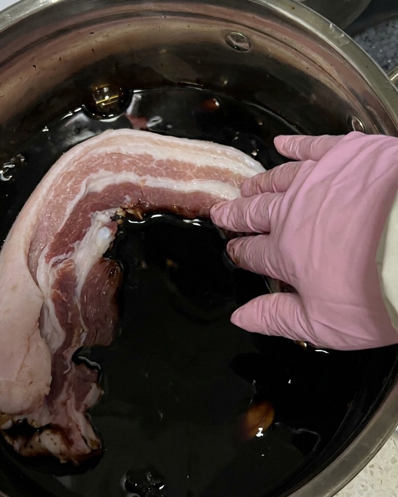 Lanières de porc cru immergées dans un récipient rempli de marinade à la sauce soja foncée.