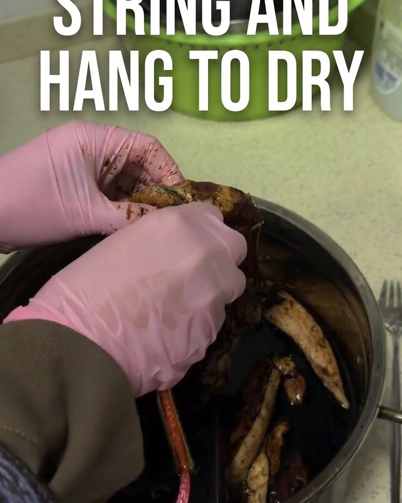 Lanière de porc mariné brun foncé attachée avec une ficelle rouge pour le séchage.