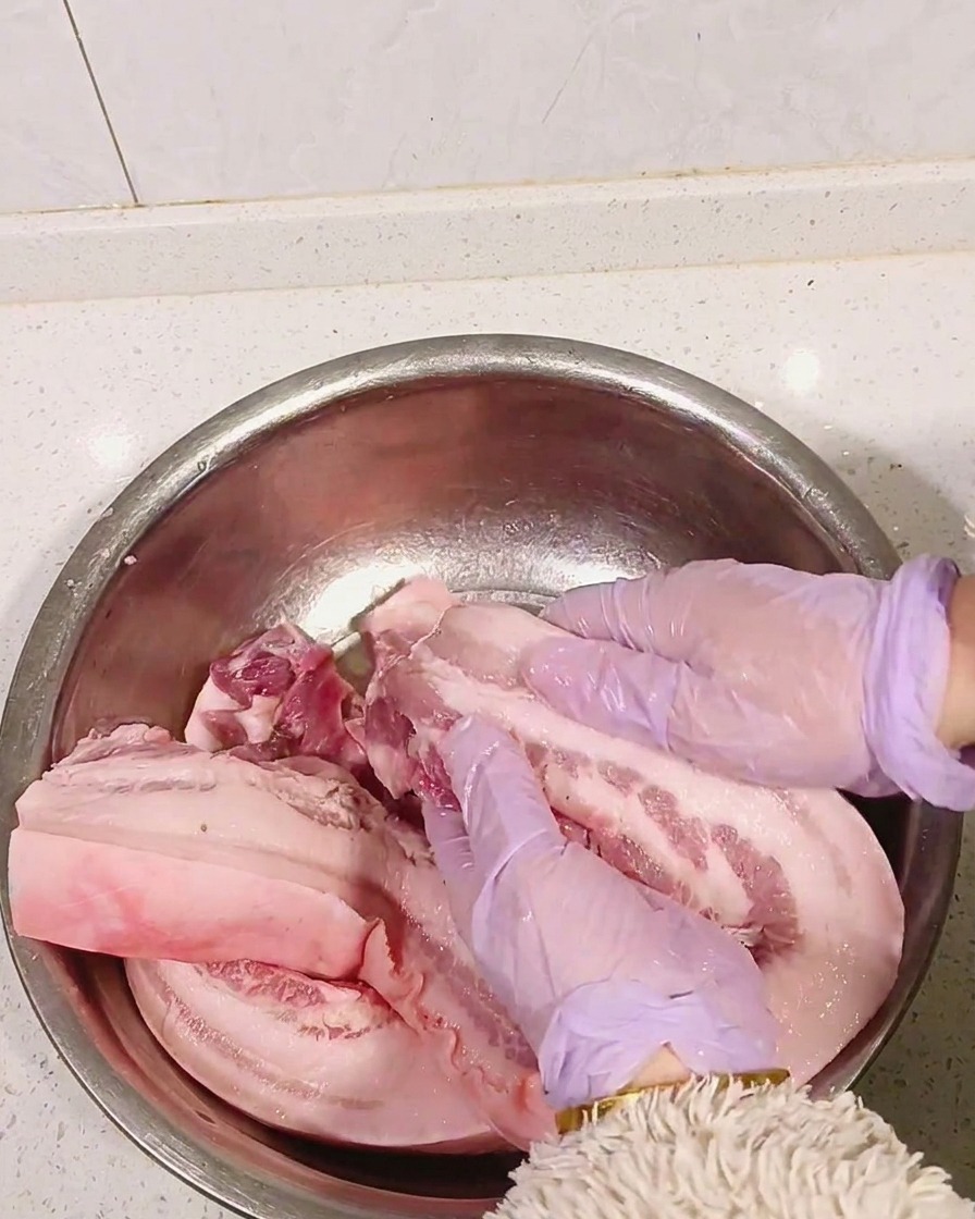 Mains gantées de violet massant lalcool blanc dans la poitrine de porc crue.