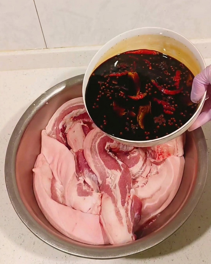 Marinade au soja refroidie versée sur la poitrine de porc dans un bol en métal.