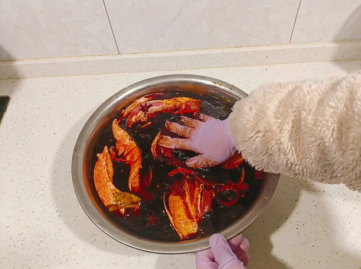 Mains gantées retournant des morceaux de poitrine de porc dans un bol de marinade au soja sombre.