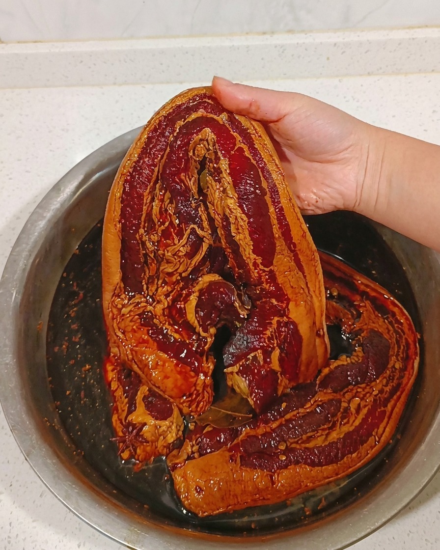 Un morceau de poitrine de porc mariné étant rincé sous un filet deau tiède.