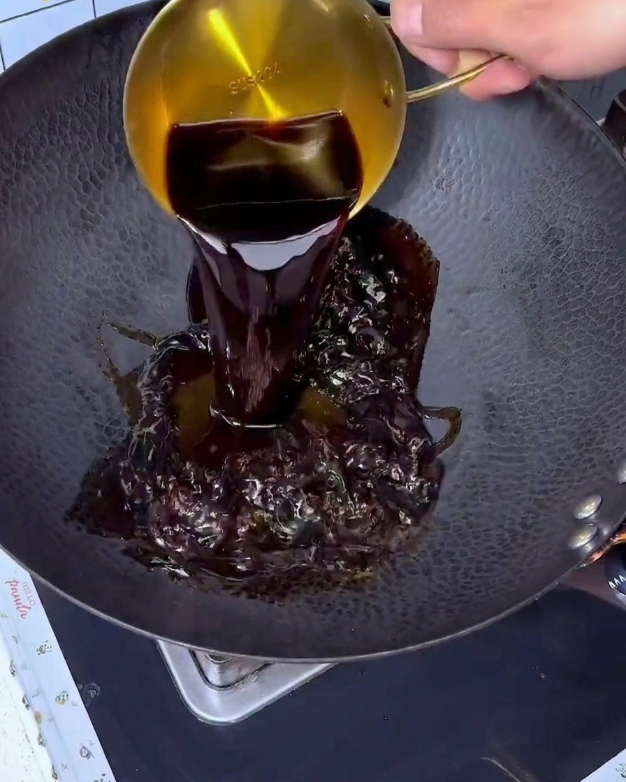 Sauce soja versée depuis une tasse à mesurer dorée dans un grand wok noir.