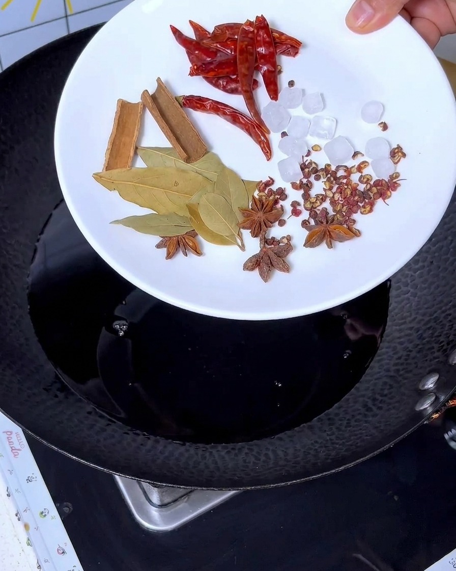 Épices comme la cannelle, lanis étoilé, le laurier, le piment et le sucre candi ajoutés au liquide sombre dans le wok.