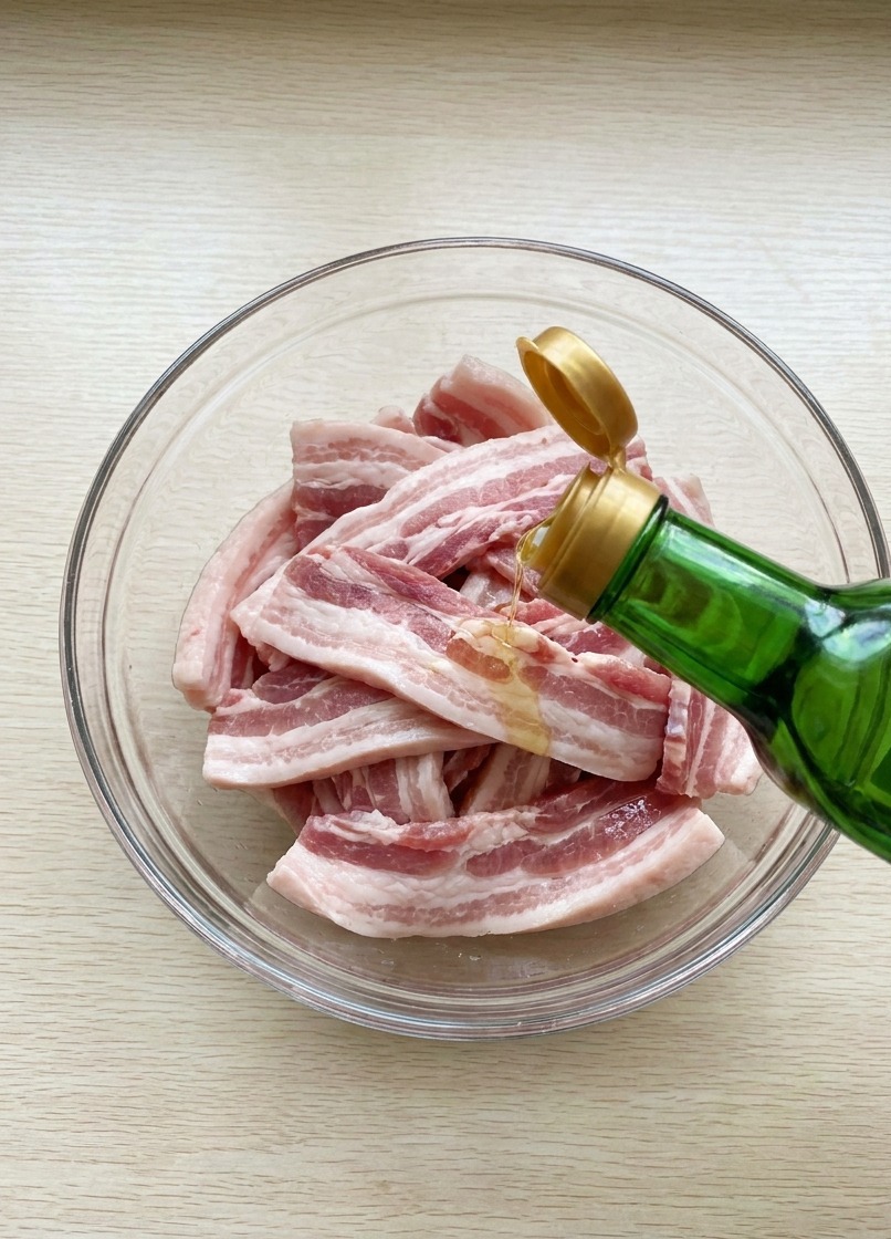 Sauce soja versée depuis une bouteille en verre sur les morceaux de porc dans un bol.