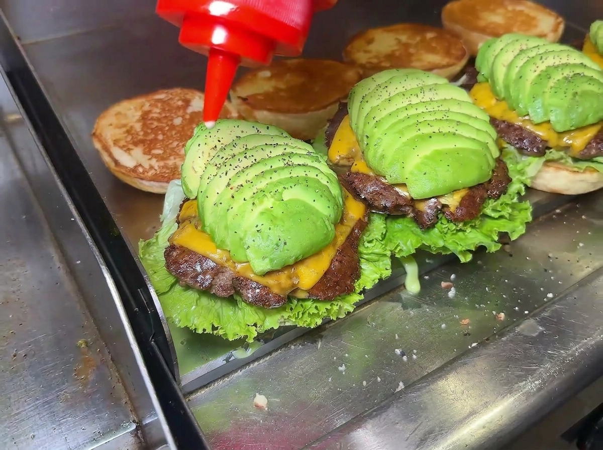 Gros plan dune main pressant un flacon pour verser de la sauce sur un magnifique cheeseburger à lavocat en cours de montage.