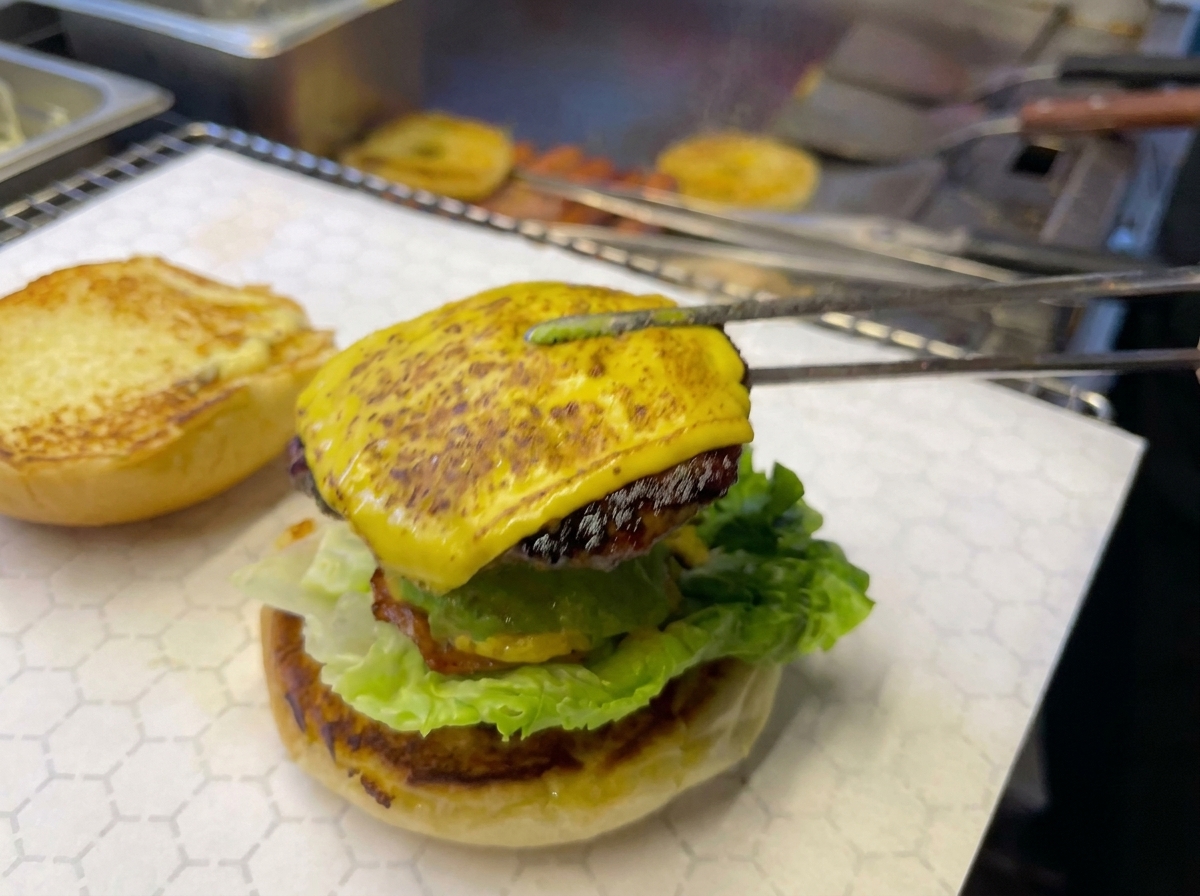 Pince de cuisine plaçant le steak au fromage et la tranche dananas sur le burger.
