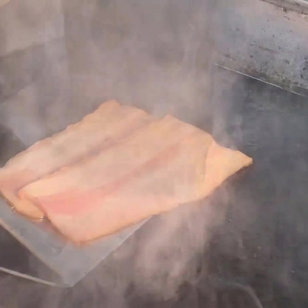 Tranches de bacon qui frire sur une plaque chaude, dégageant de la vapeur.