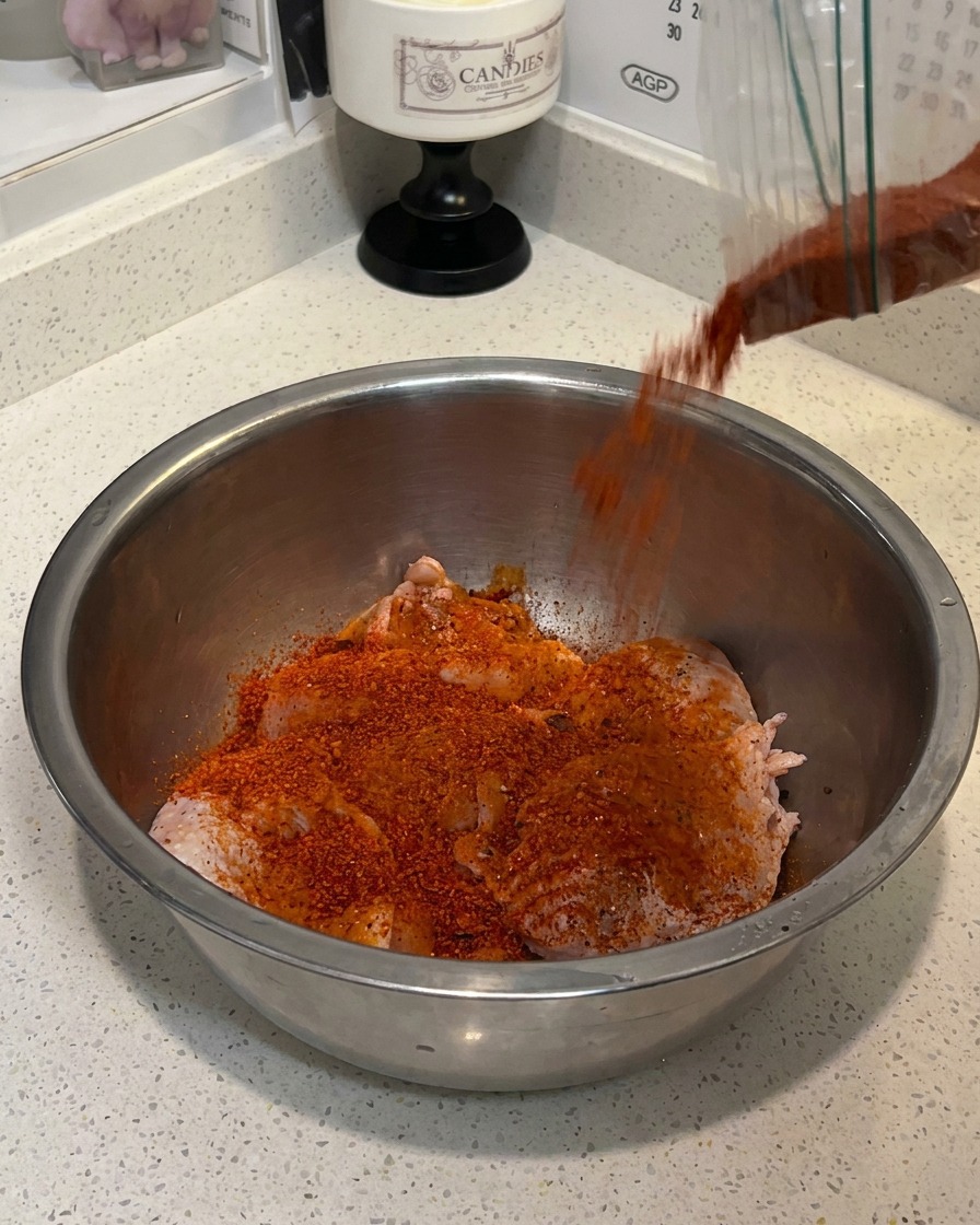 Hauts de cuisse de poulet crus assaisonnés avec de la poudre dépices et du lait dans un grand bol en métal.