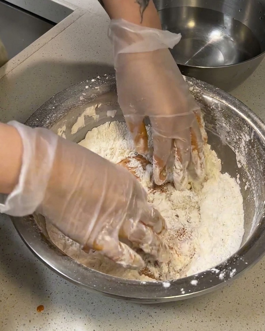 Poulet mariné pressé fermement dans un bol de farine pour la première couche de panure.