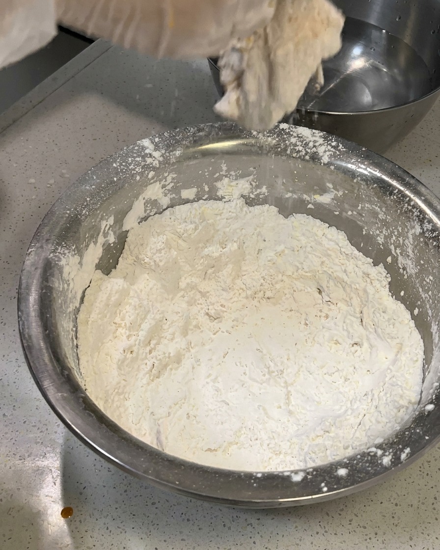 Le morceau de poulet réhydraté en train dêtre délicatement recoiffé de farine pour créer une texture floconneuse.