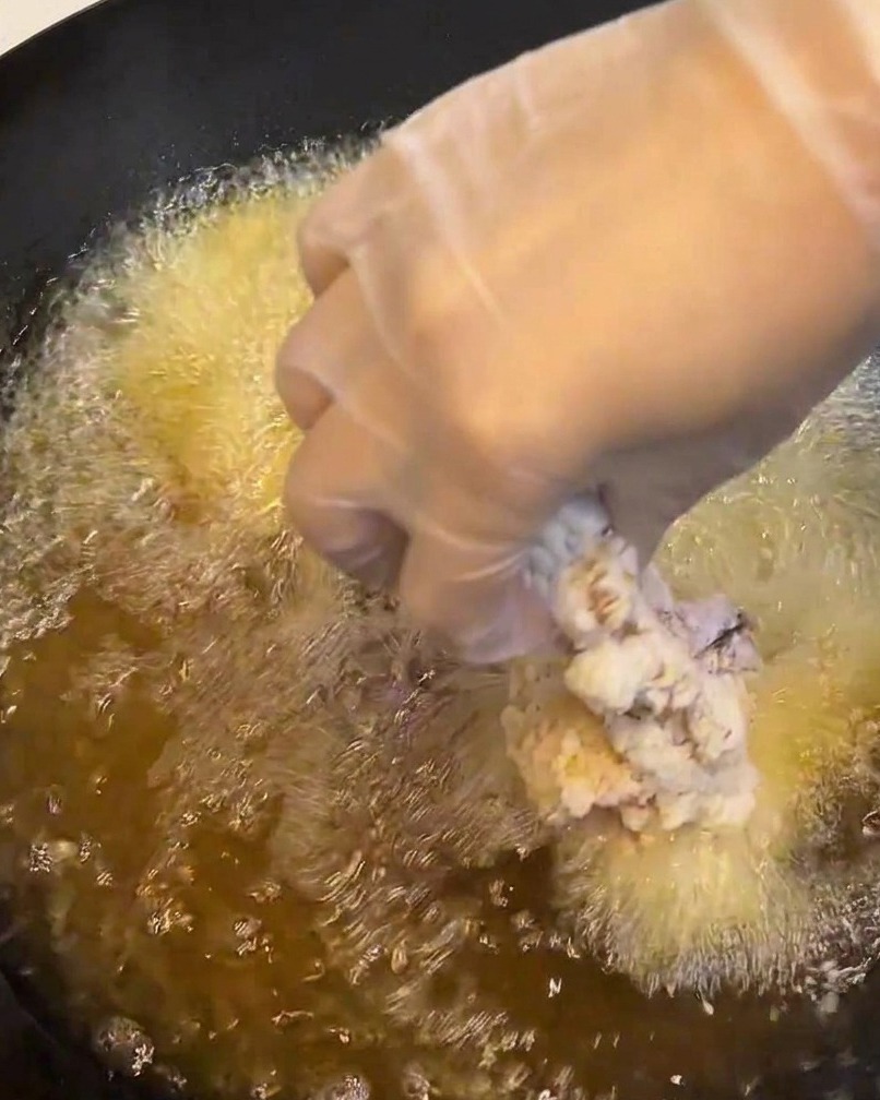 Un morceau de poulet pané plongé dans une casserole dhuile chaude et bouillonnante.