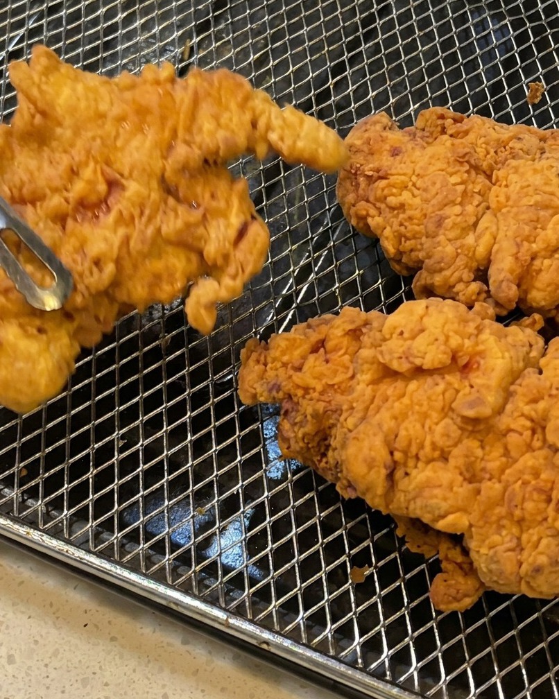 Poulet frit retiré de lhuile avec des pinces, montrant une panure croustillante.