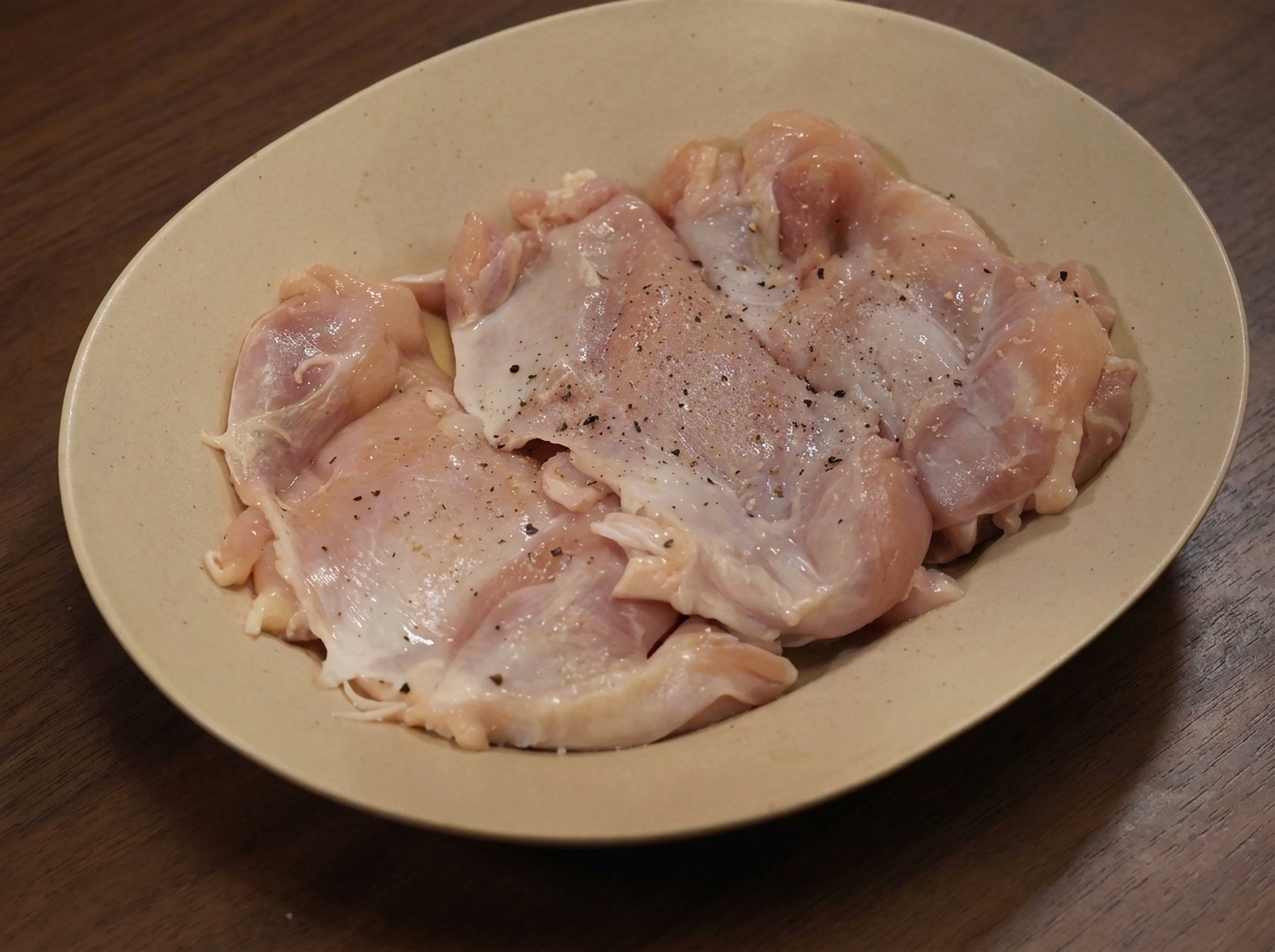 Hauts de cuisse de poulet crus sur une assiette, saupoudrés dépices diverses.