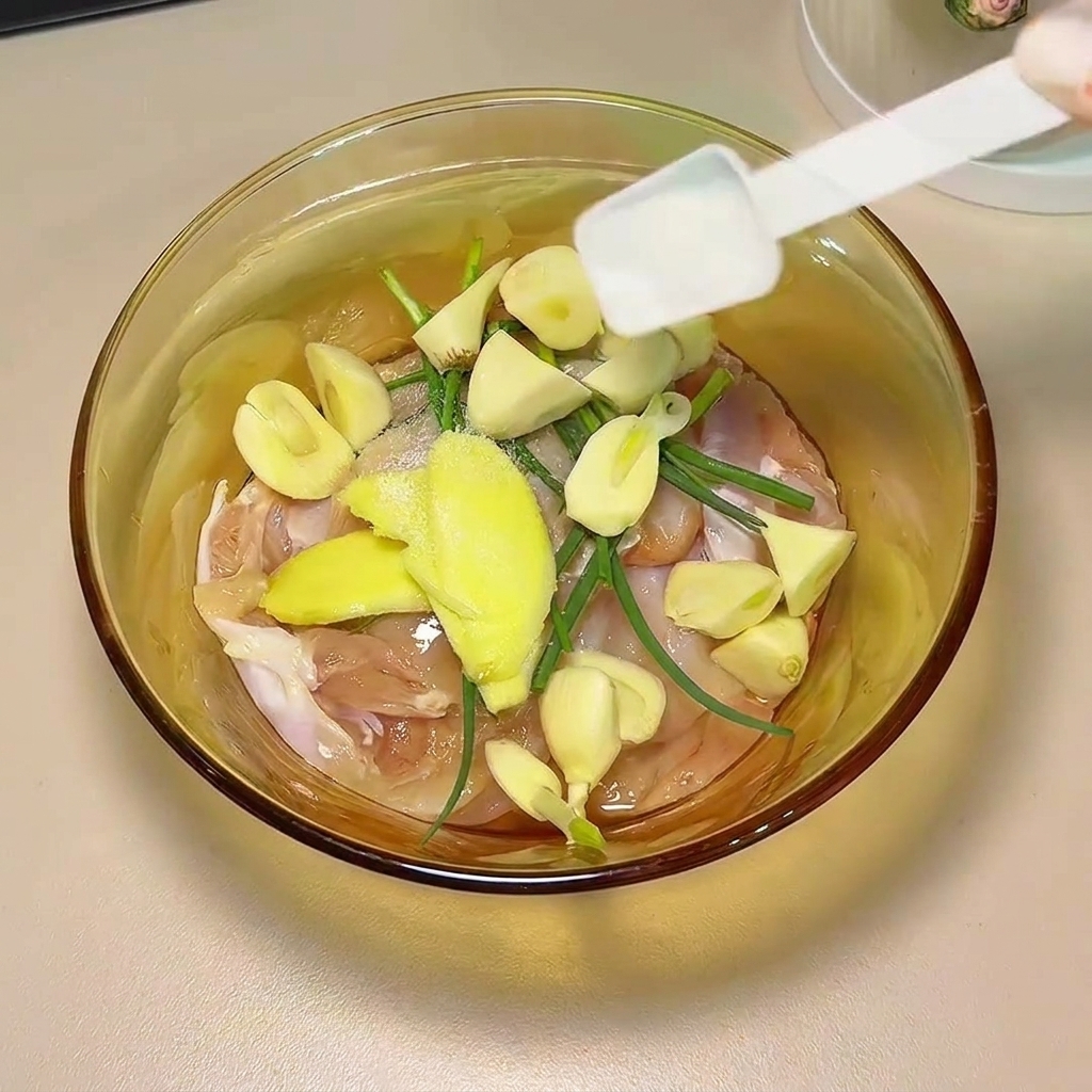 La sauce soja et les épices versées sur le poulet et les aromates dans un bol en verre.