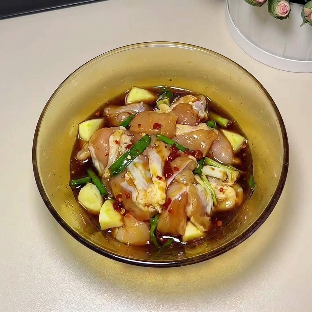 Des hauts de cuisse de poulet crus massés à la main avec les ingrédients de la marinade dans un bol en verre.