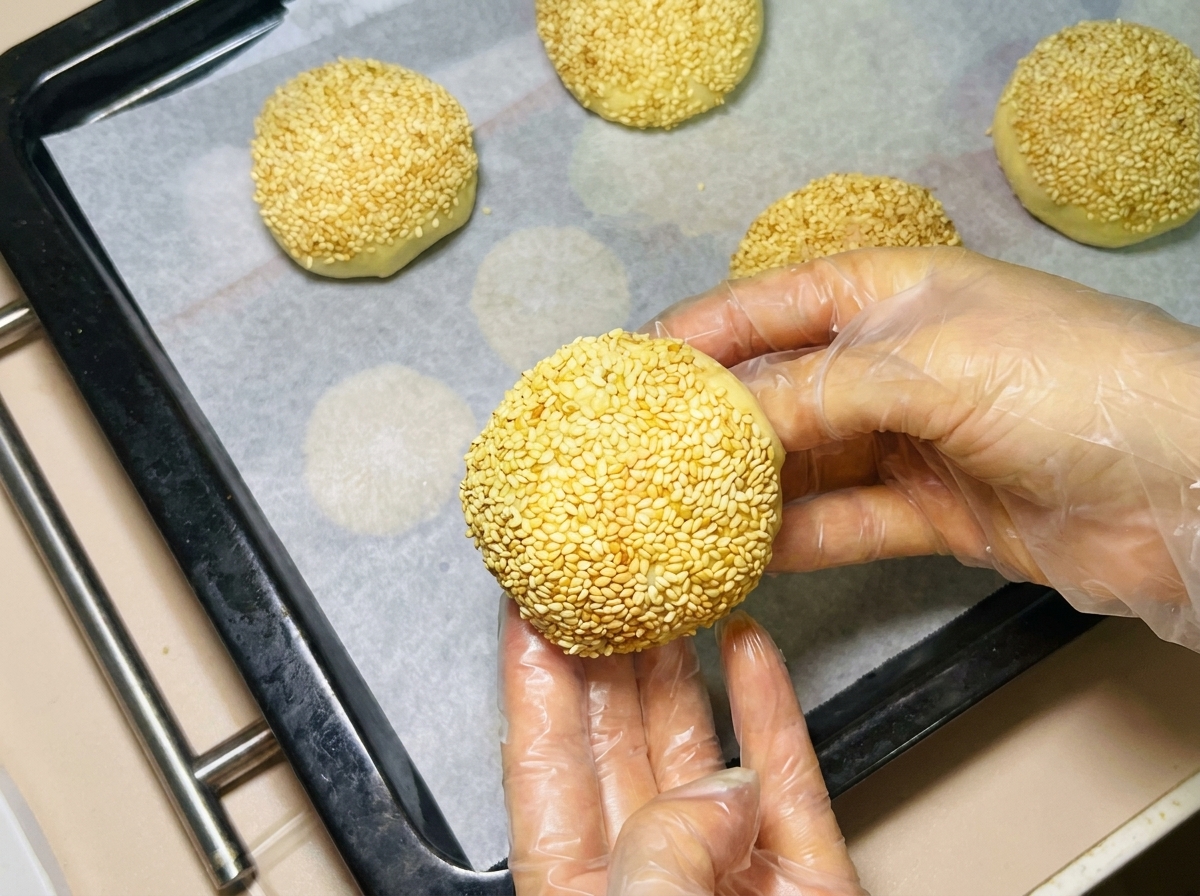 Une main gantée disposant une boule de pâte au sésame sur une plaque de cuisson tapissée de papier sulfurisé.