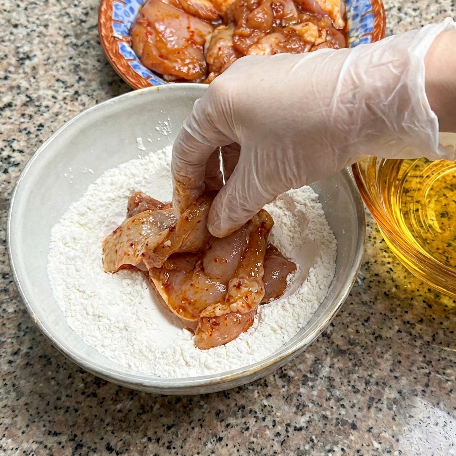 Une cuisse de poulet marinée pressée dans un bol de farine.