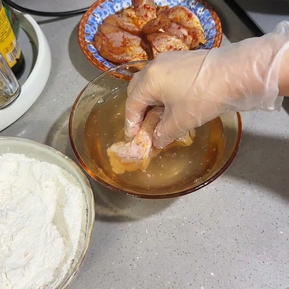 Une cuisse de poulet farinée brièvement immergée dans un bol deau.