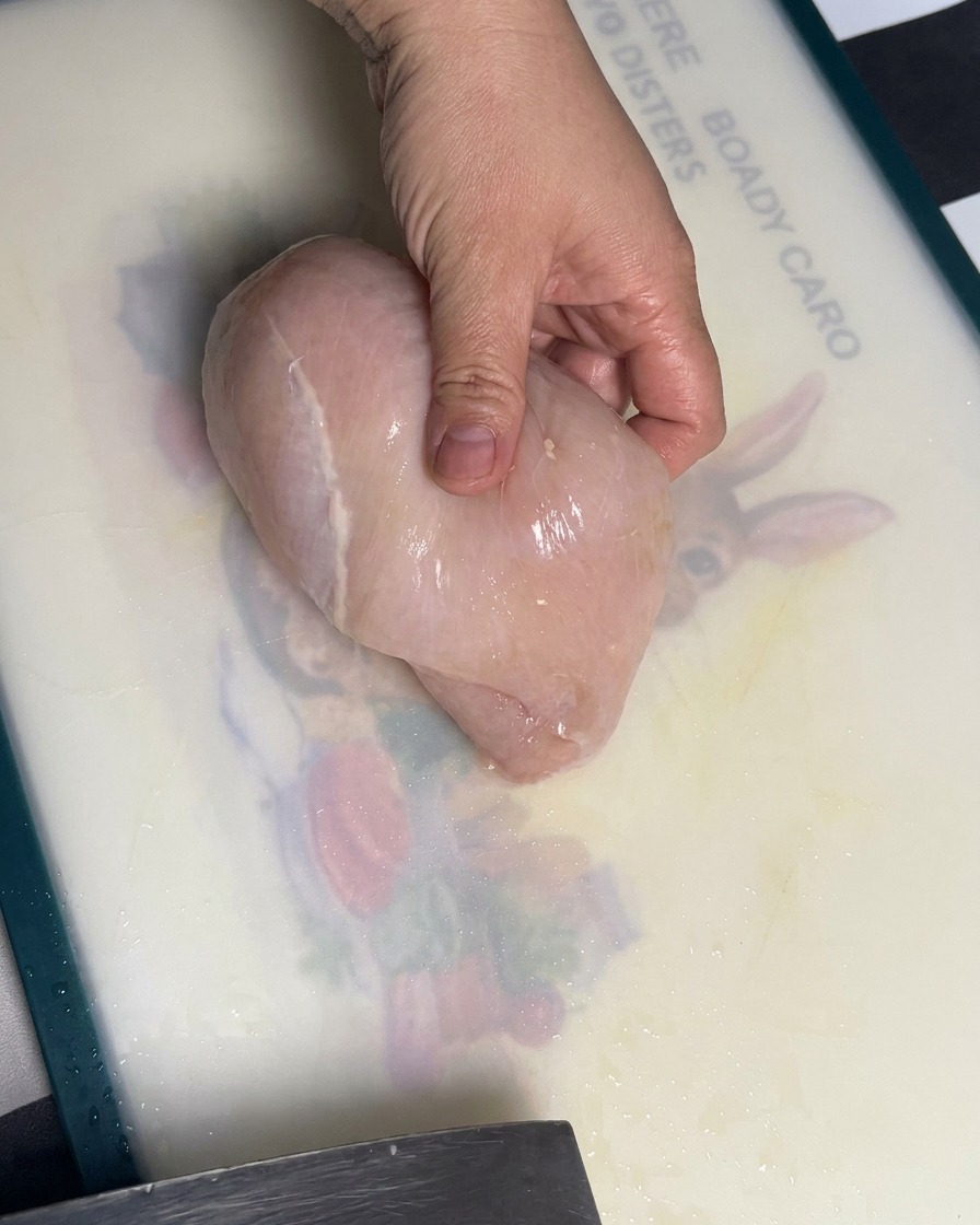 Un blanc de poulet cru en cours de tranchage en morceaux réguliers sur une planche à découper.