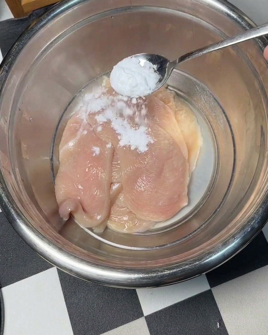 Du bicarbonate de soude saupoudré sur des tranches de poulet cru dans un bol en métal.