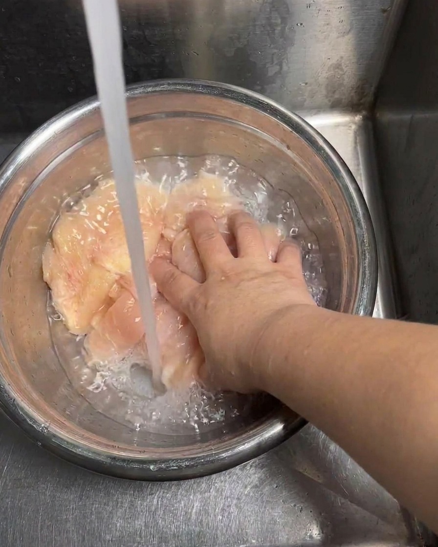 Des tranches de poulet cru rincées sous un jet deau froide.