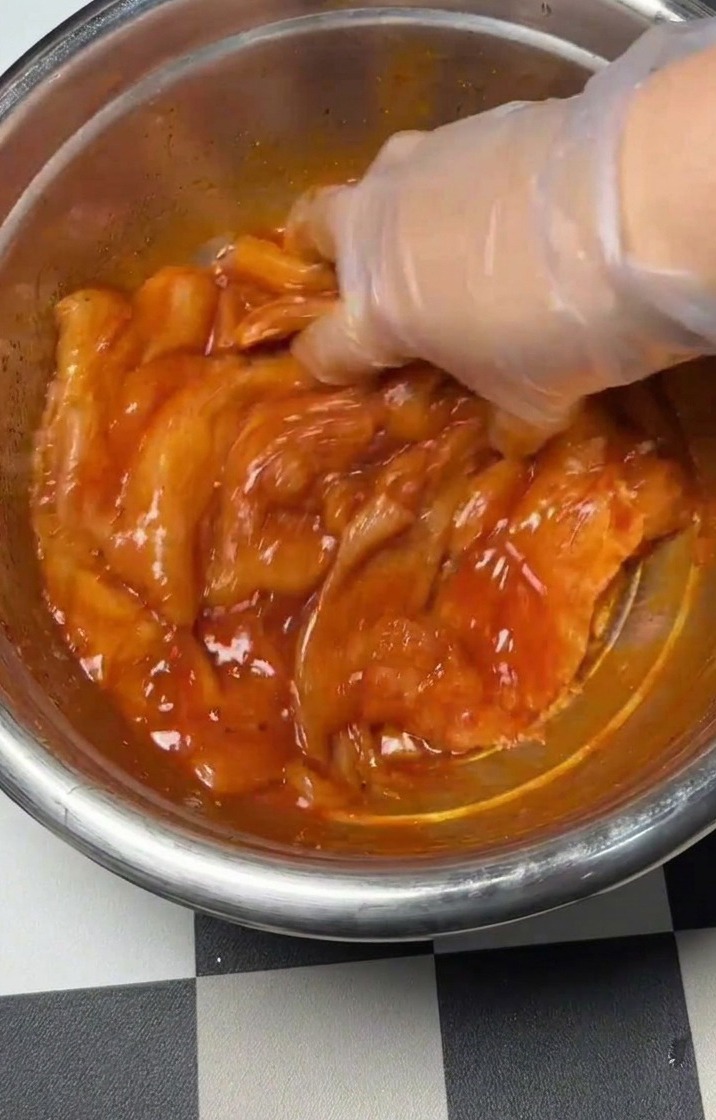 Une main mélangeant le poulet, lœuf et les épices dans un bol en métal.