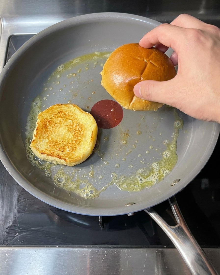 Pains à burger dans une poêle avec du beurre fondu en train de dorer.