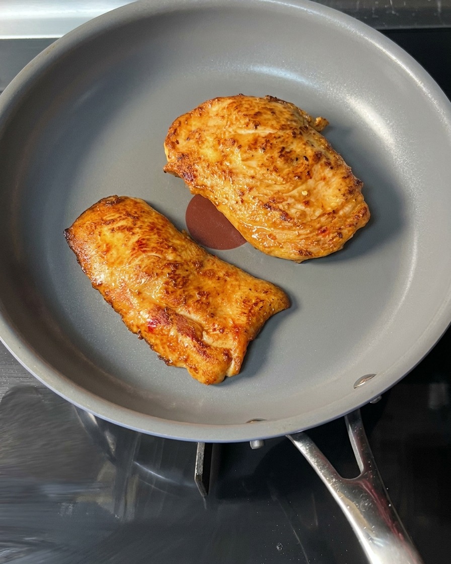 Un steak de poulet doré et cuit soulevé par une pince rouge.