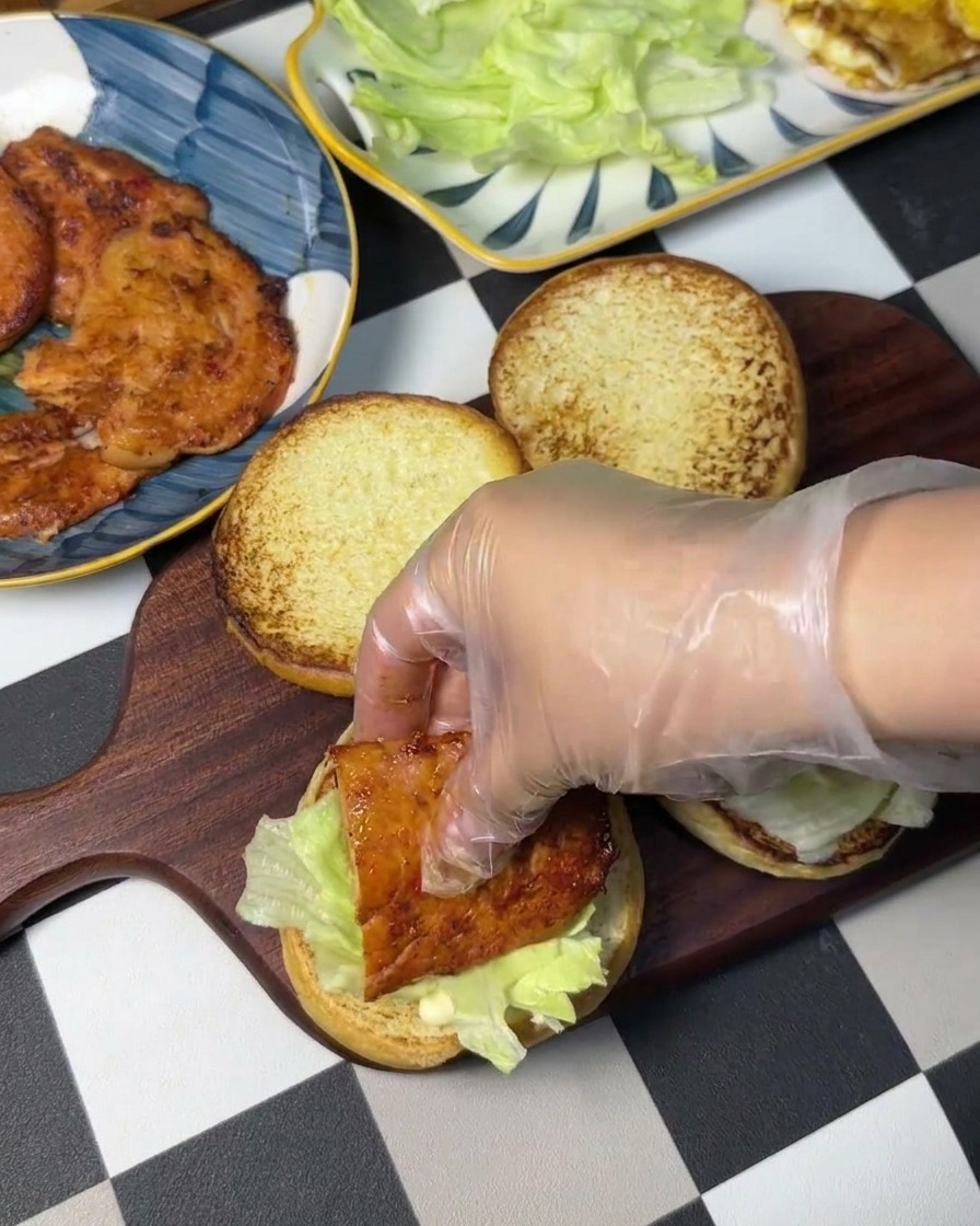 Une main gantée plaçant un steak de poulet sur un lit de laitue fraîche.