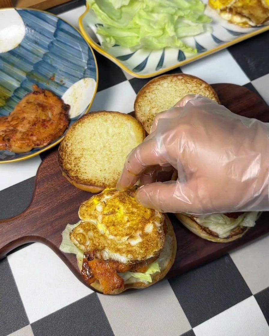 Une main gantée plaçant un œuf au plat sur le steak de poulet.