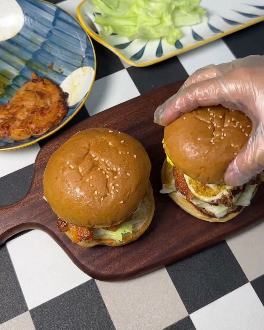 Une main gantée posant le chapeau du burger sur lempilement.