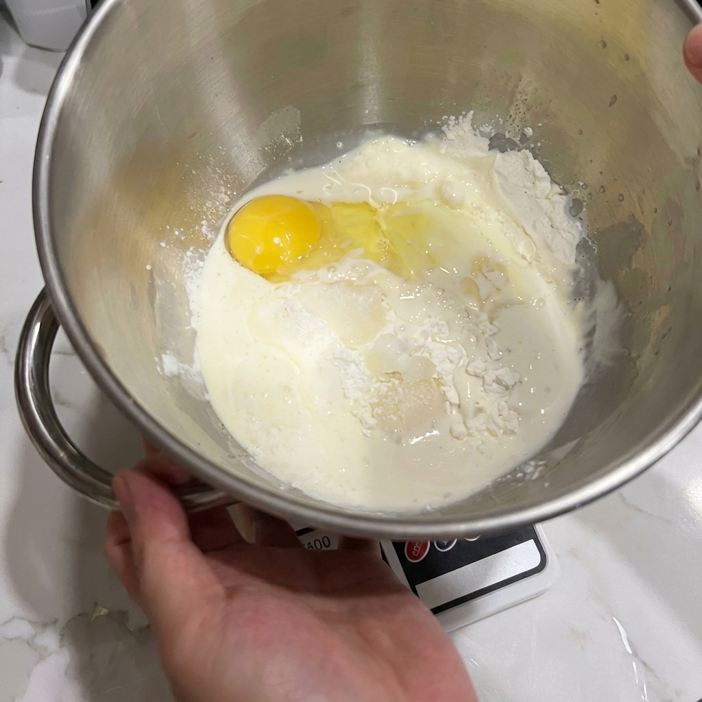 Un bol de robot pâtissier contenant de la farine, un œuf et du lait.