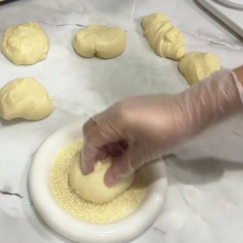 Une main plaçant une boule de pâte dans une assiette de graines de sésame.