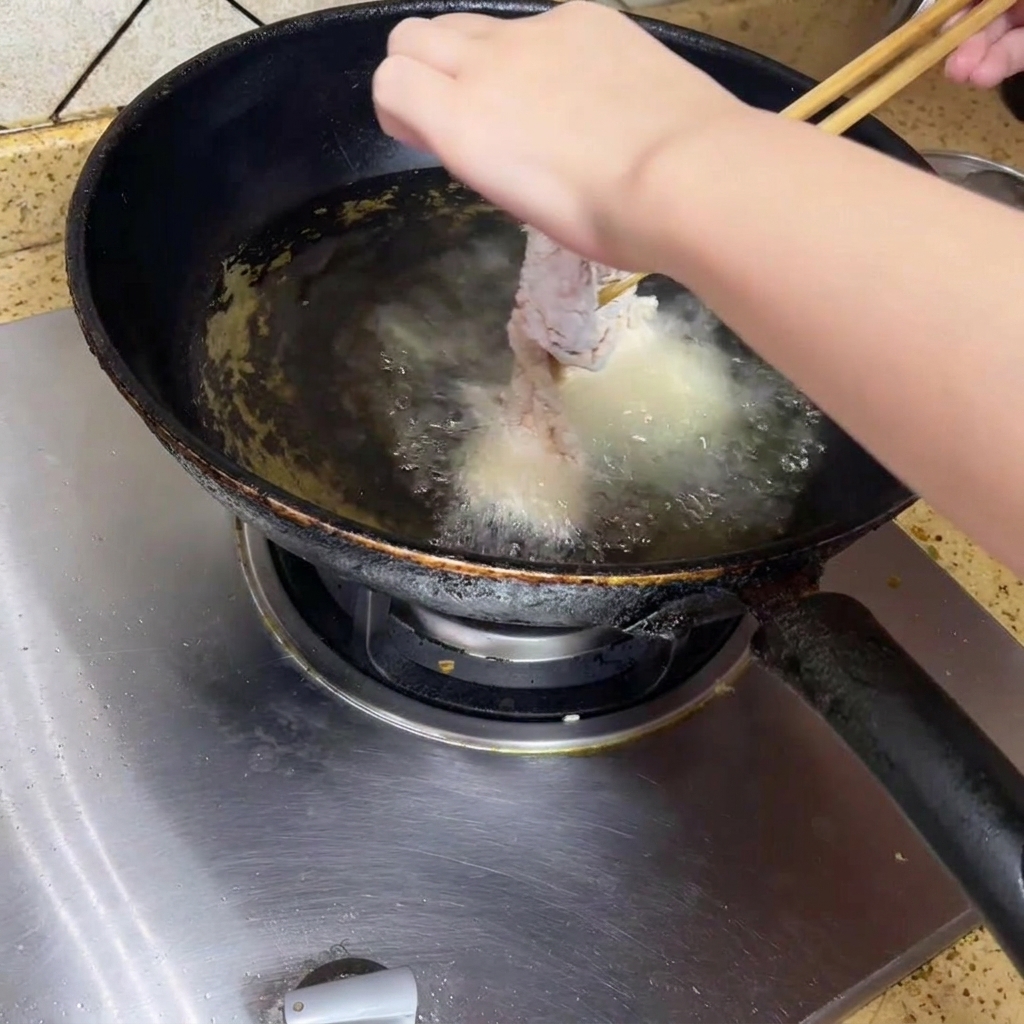Morceau de poulet plongé dans de lhuile bouillante dans un wok.