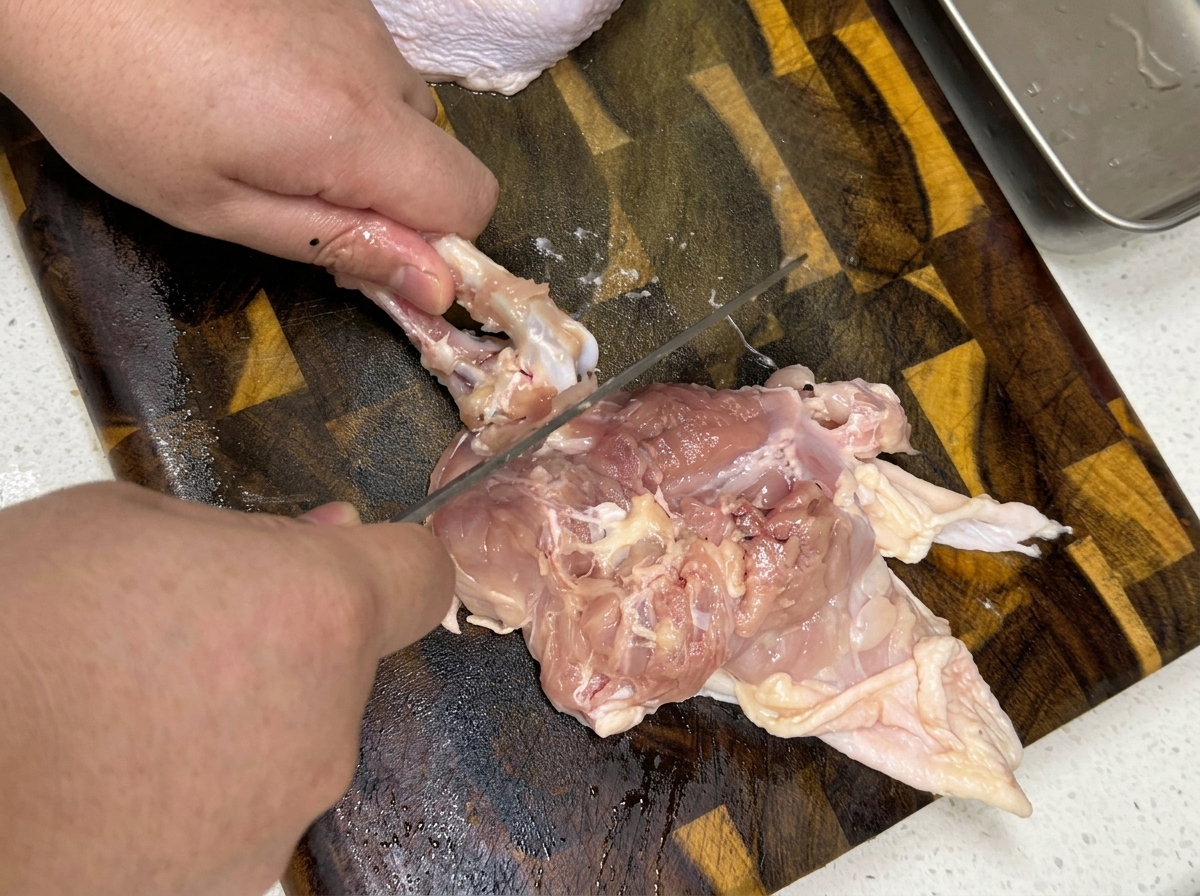 Gros plan sur des mains désossant une cuisse de poulet crue sur une planche à découper en bois.