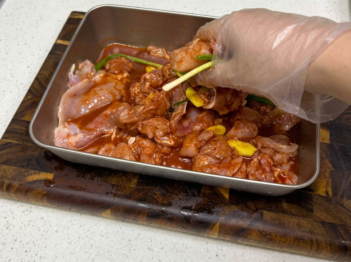 Mains mélangeant la marinade aux morceaux de poulet.