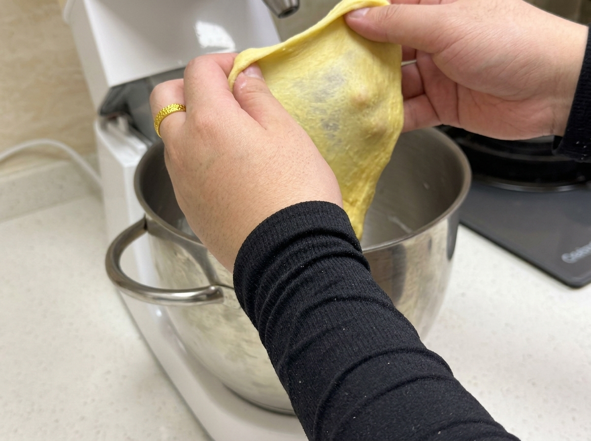 Un morceau de pâte jaune étiré montrant une fine membrane élastique.