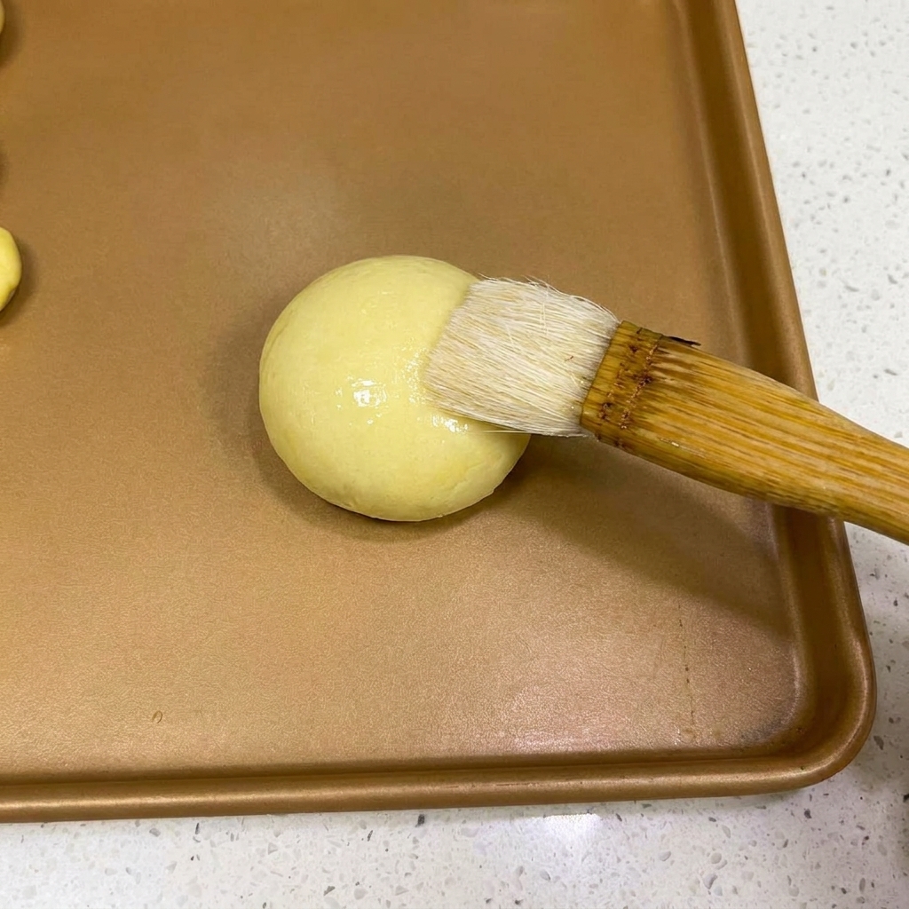 Un pinceau appliquant une fine couche deau sur le dessus dune boule de pâte.